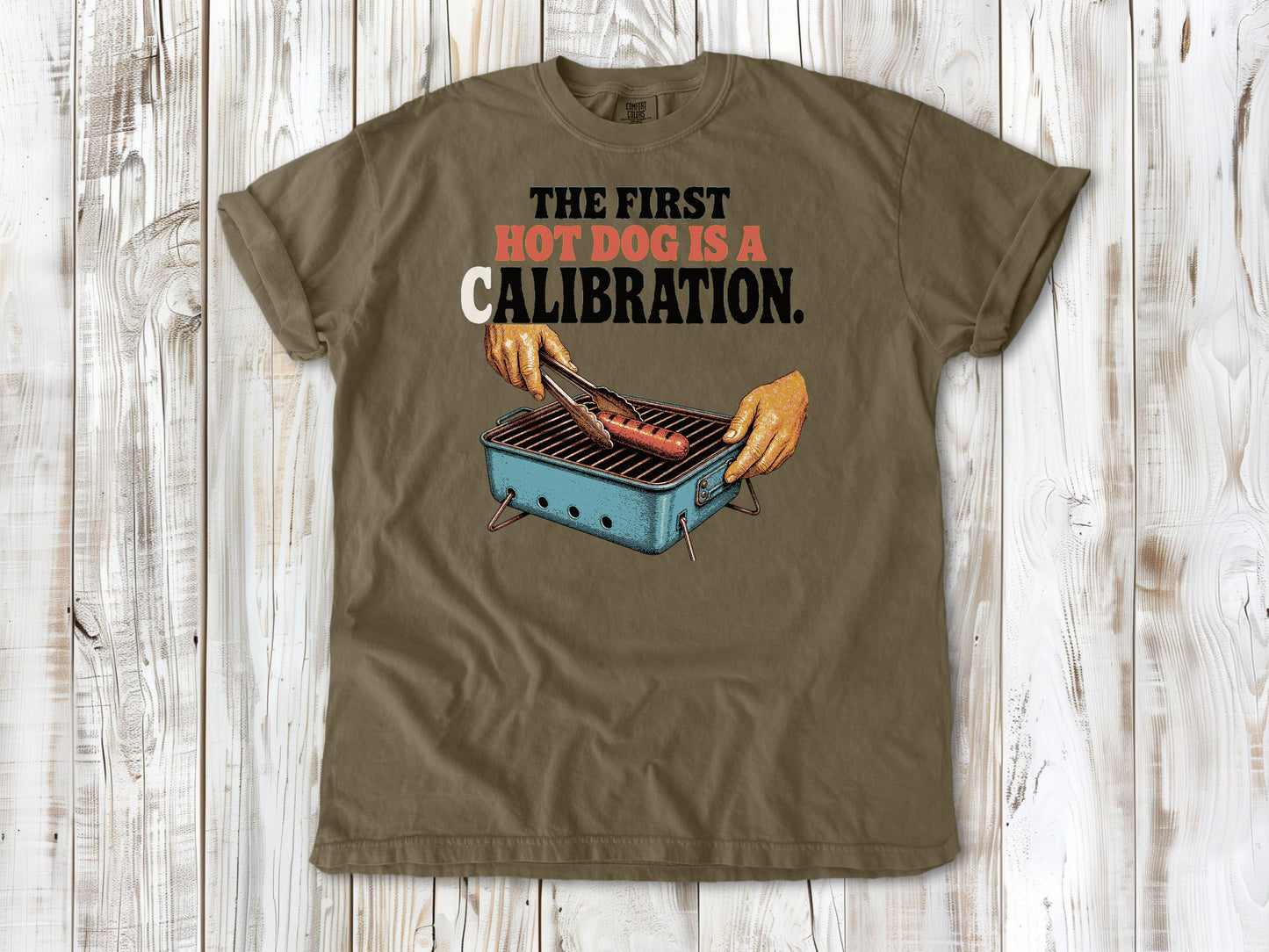 Graphite garment-dyed tee with The First Hot Dog Is a Calibration beach grilling graphic.