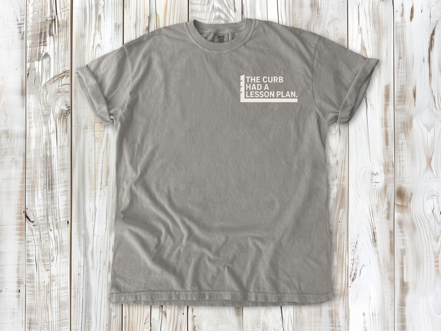 Grey garment-dyed tee with The Curb Had a Lesson Plan small left-chest skate graphic.