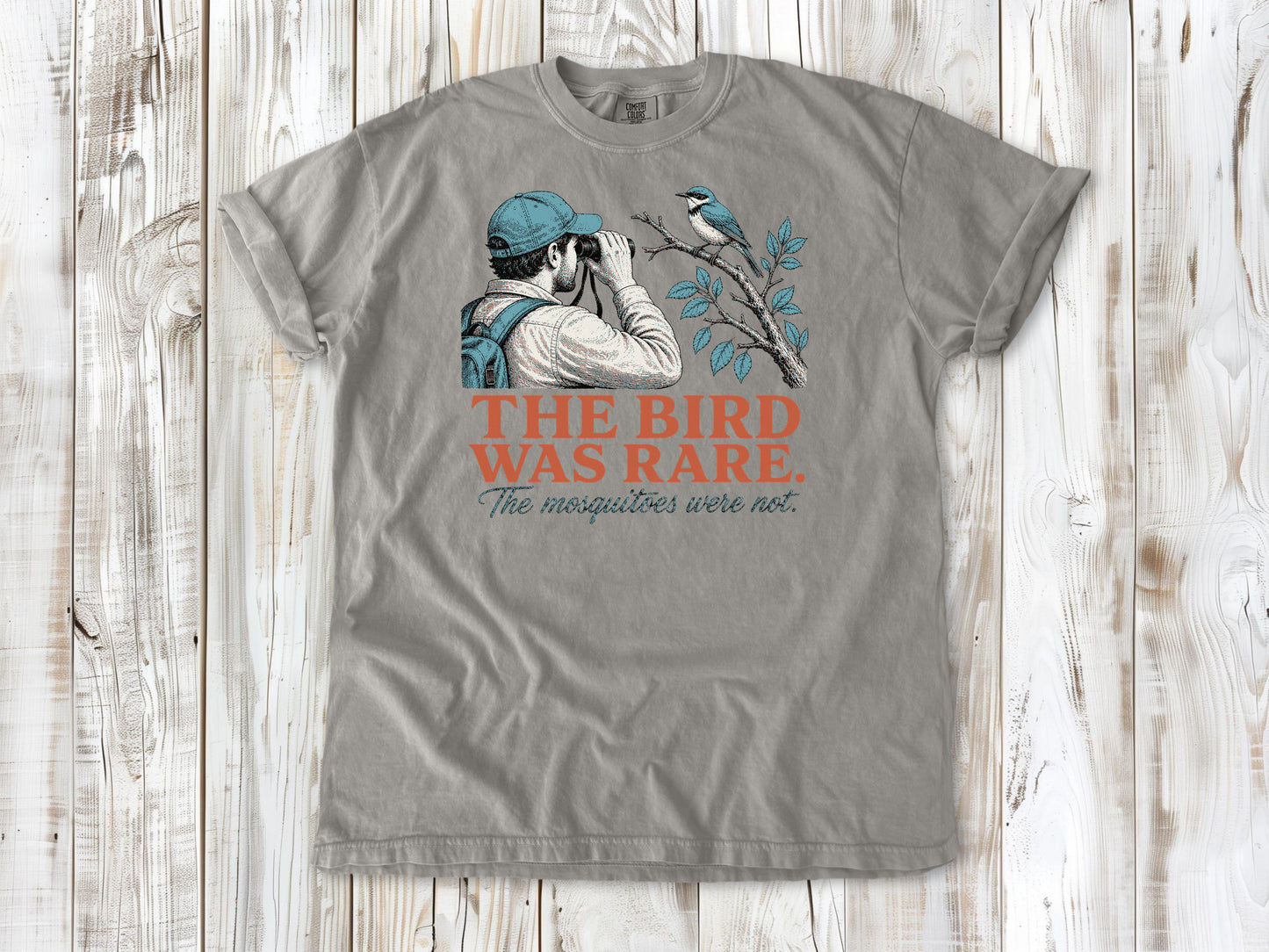 Khaki garment-dyed tee with The Bird Was Rare The Mosquitoes Were Not birdwatching graphic.