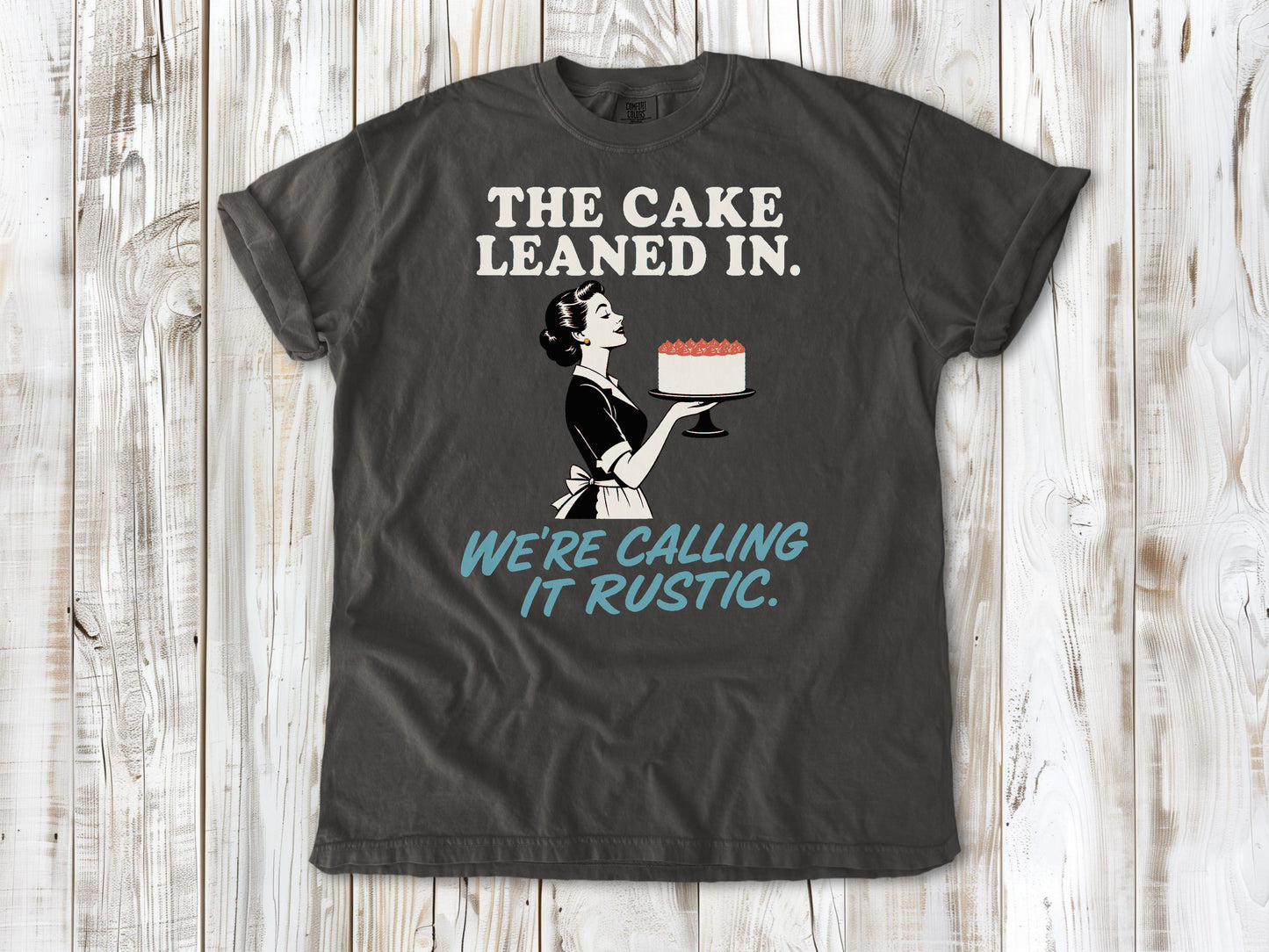 Ivory garment-dyed tee with The Cake Leaned In We're Calling It Rustic baking graphic.