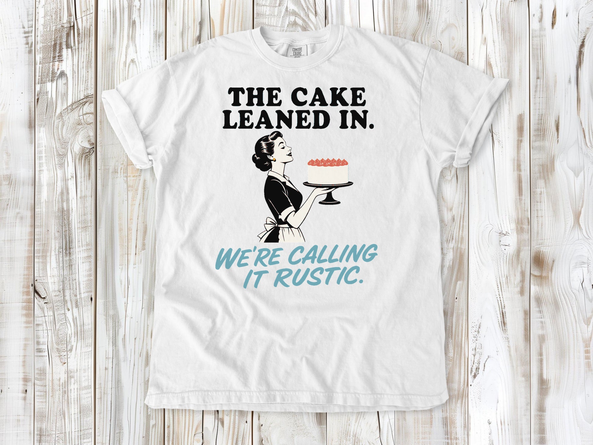White garment-dyed tee with The Cake Leaned In We're Calling It Rustic baking graphic.