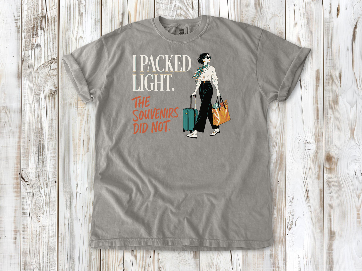 Khaki garment-dyed tee with I Packed Light The Souvenirs Did Not travel graphic.