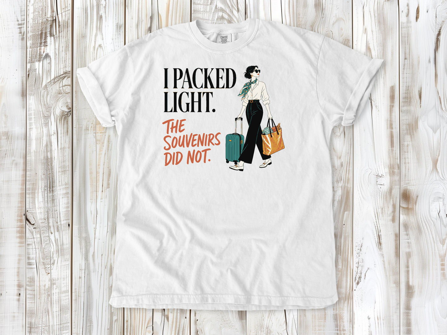 White garment-dyed tee with I Packed Light The Souvenirs Did Not travel graphic.