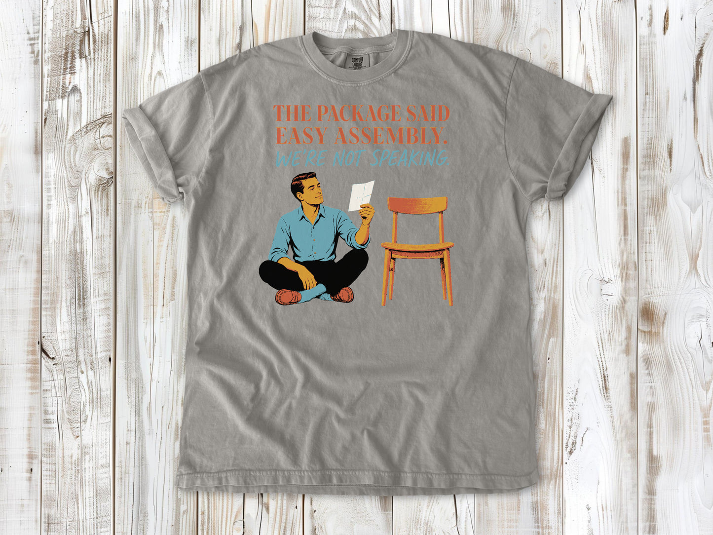Khaki garment-dyed tee with The Package Said Easy Assembly We're Not Speaking DIY graphic.