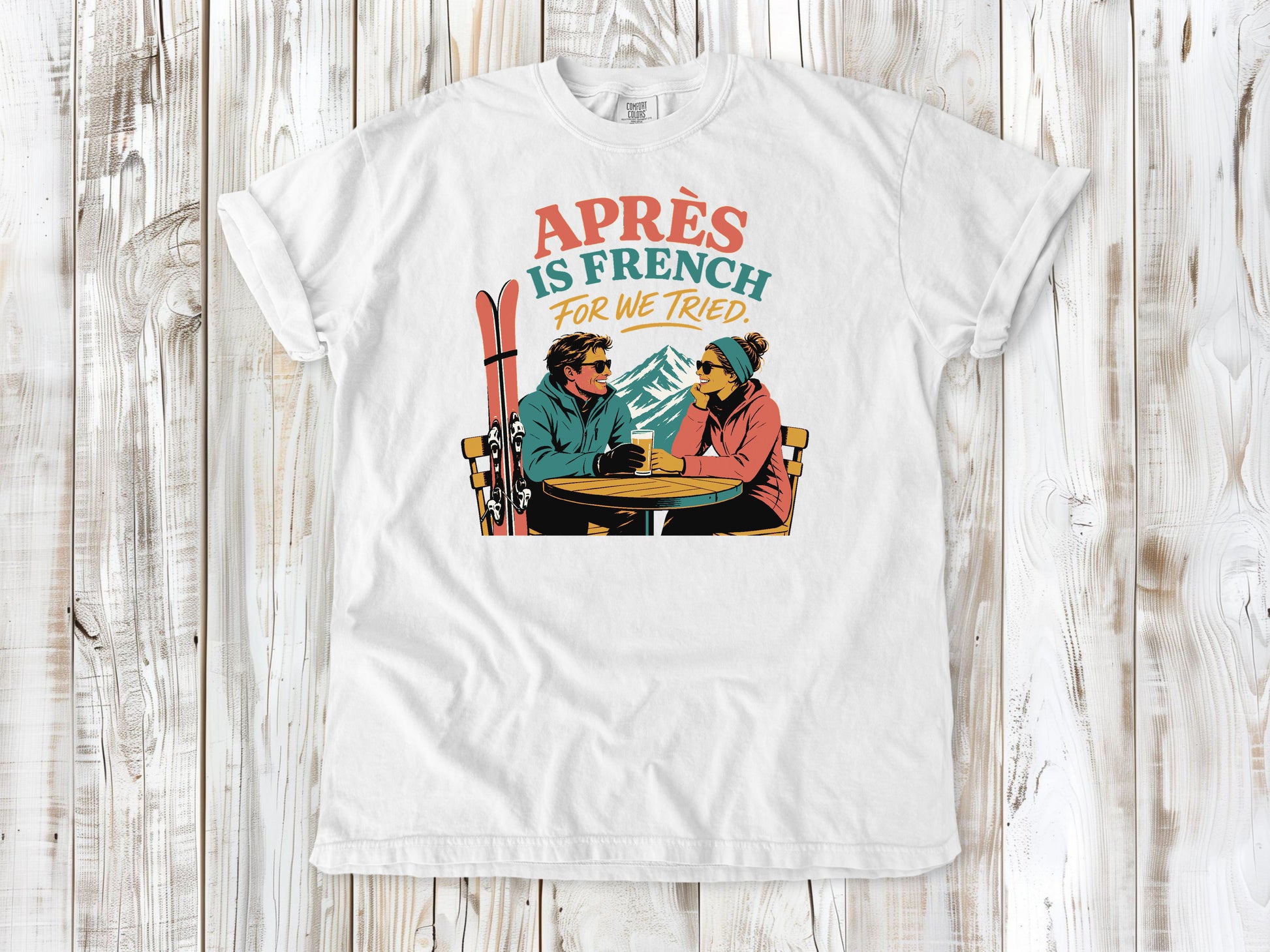 White garment-dyed tee with Après Is French for We Tried skiing graphic.