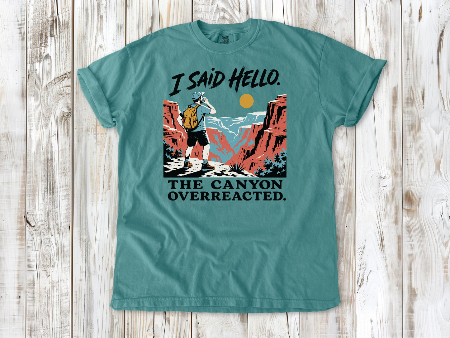 Mustard garment-dyed tee with I Said Hello The Canyon Overreacted hiking graphic.