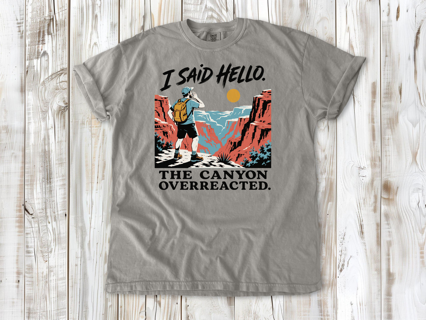 Khaki garment-dyed tee with I Said Hello The Canyon Overreacted hiking graphic.