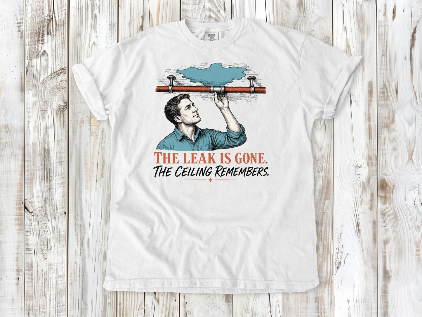 White garment-dyed tee with The Leak Is Gone The Ceiling Remembers home repair graphic.