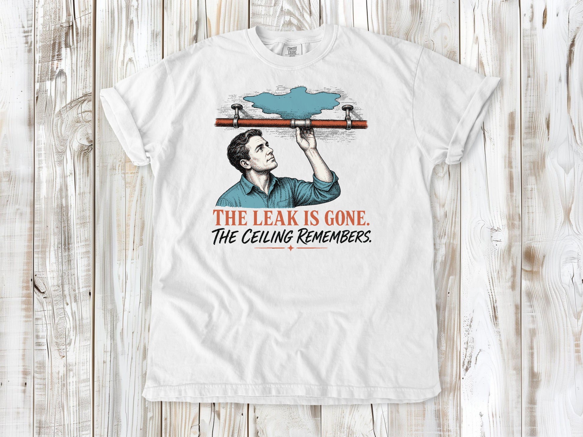 White garment-dyed tee with The Leak Is Gone The Ceiling Remembers home repair graphic.