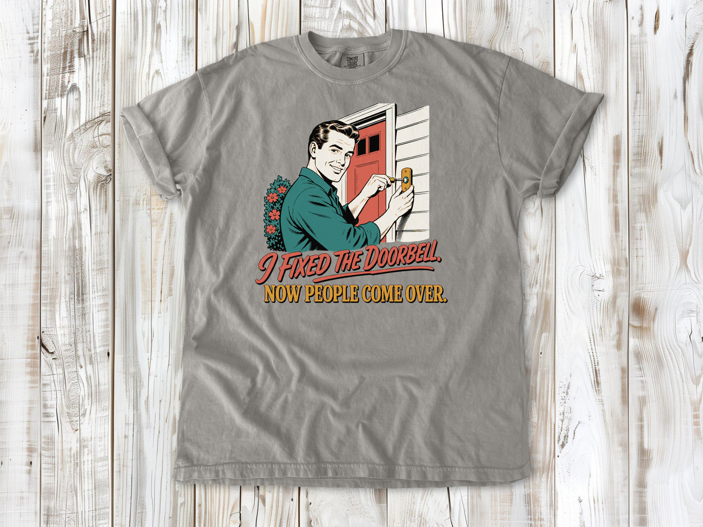 Khaki garment-dyed tee with I Fixed the Doorbell Now People Come Over DIY graphic.
