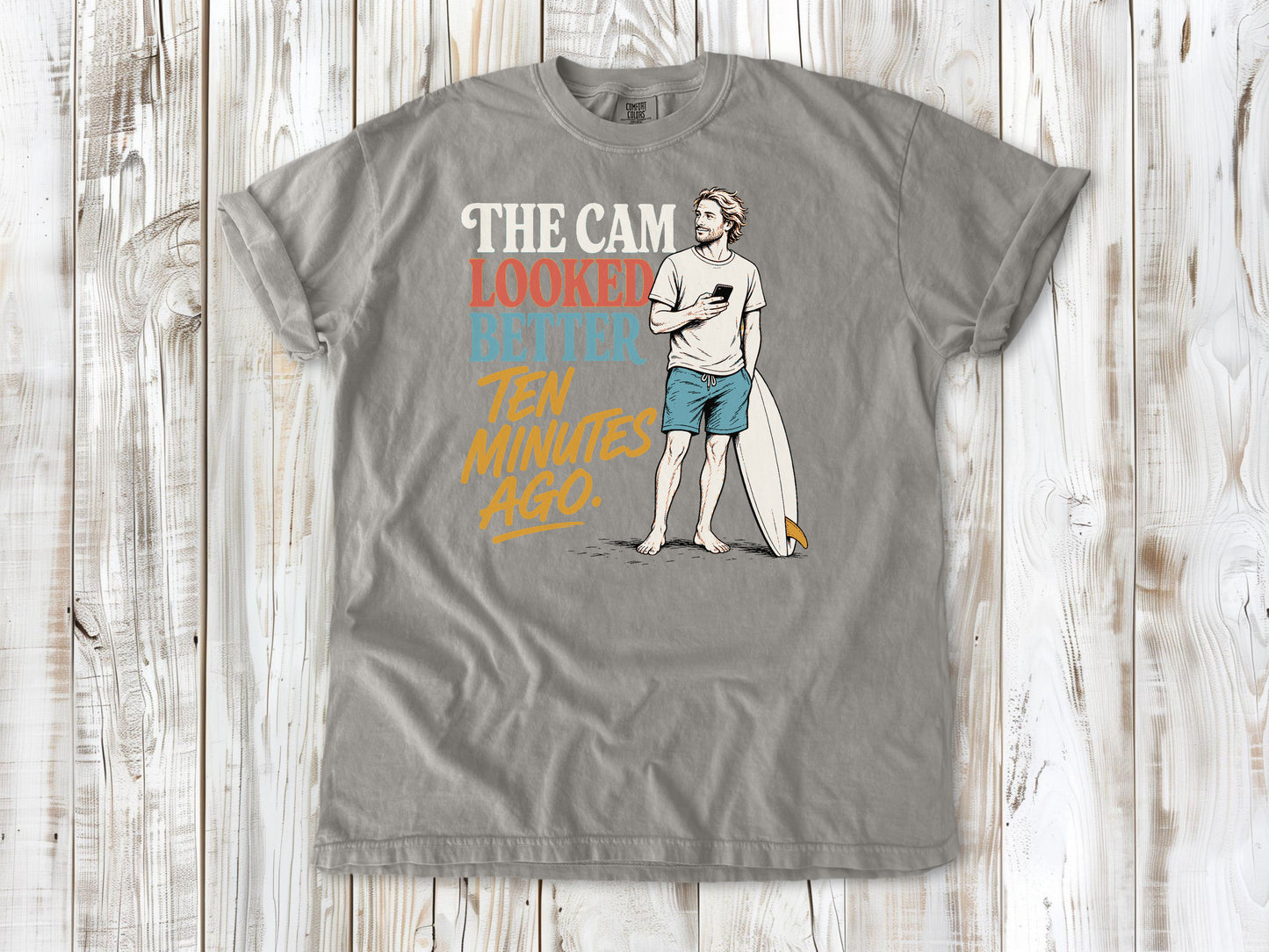 Khaki garment-dyed tee with The Cam Looked Better Ten Minutes Ago surfer graphic.