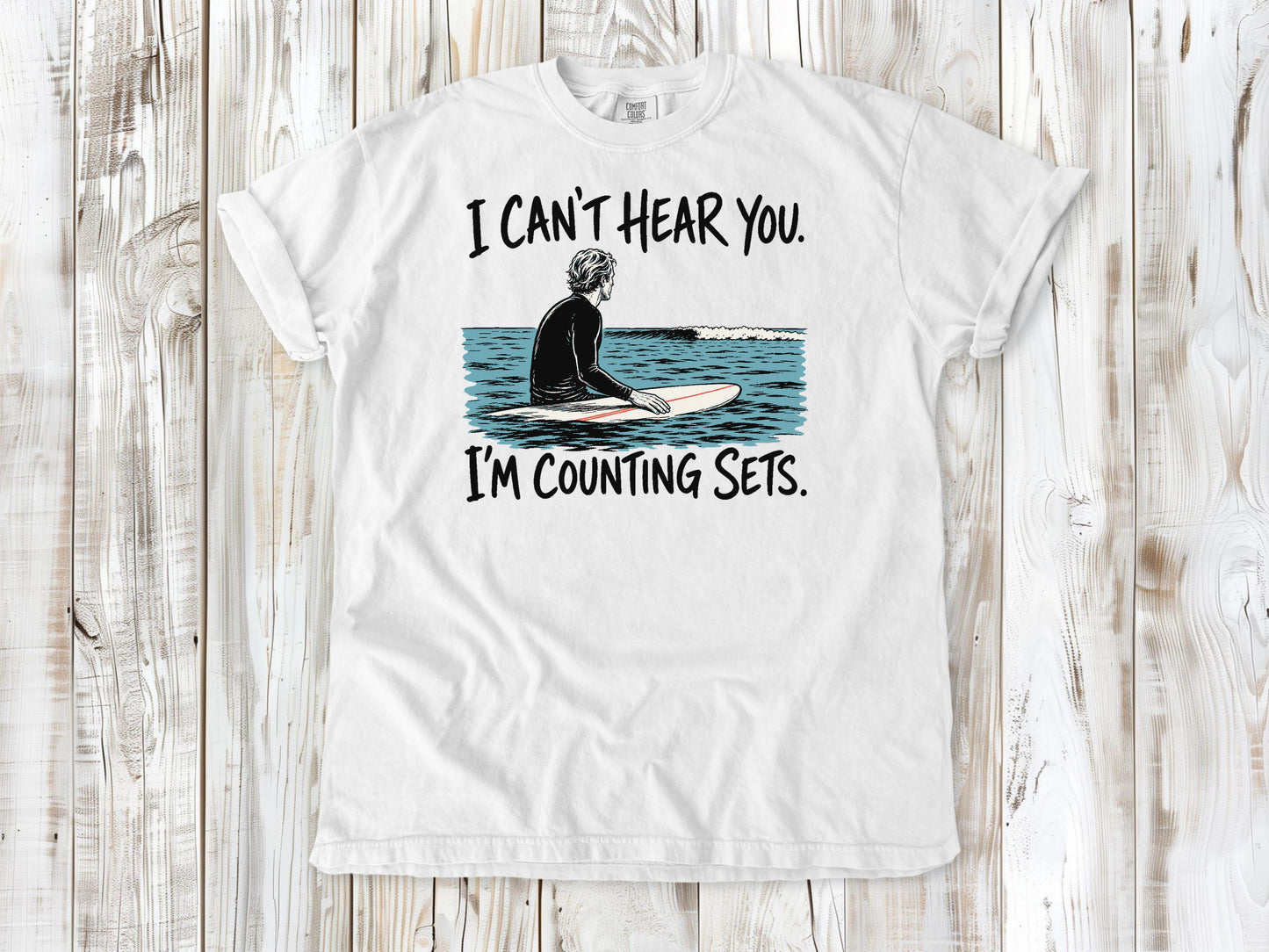 White garment-dyed tee with I Can't Hear You I'm Counting Sets surfer graphic.