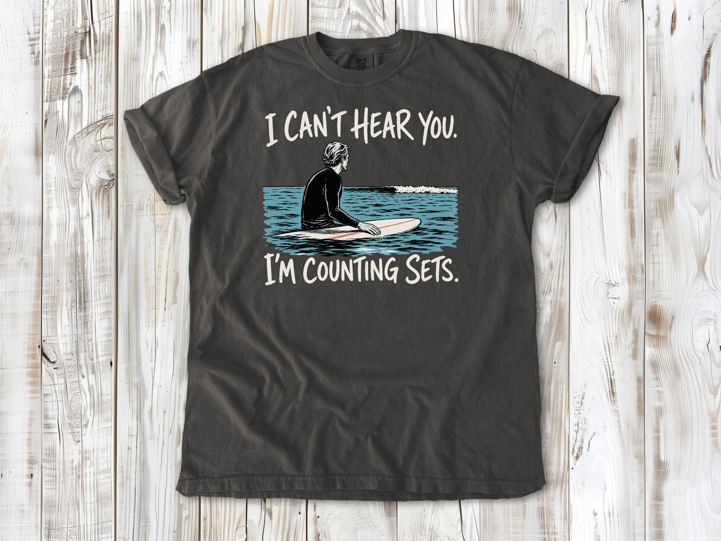 Ivory garment-dyed tee with I Can't Hear You I'm Counting Sets surfer graphic.