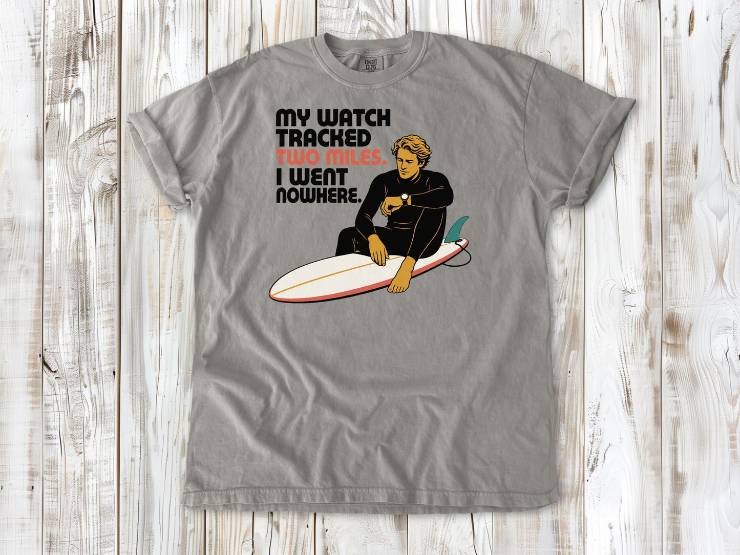 Khaki garment-dyed tee with My Watch Tracked Two Miles I Went Nowhere surfer graphic.
