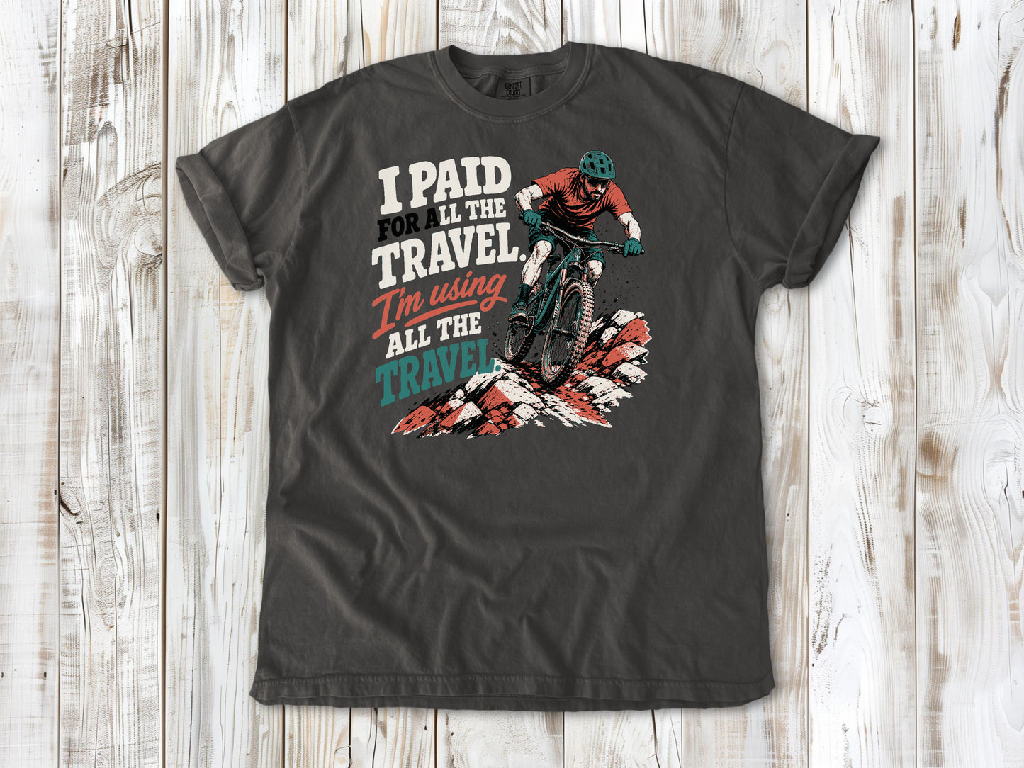 Ivory garment-dyed tee with I Paid for All the Travel mountain bike graphic.