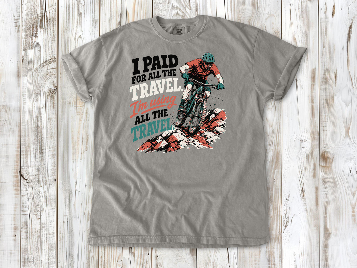 Khaki garment-dyed tee with I Paid for All the Travel mountain bike graphic.