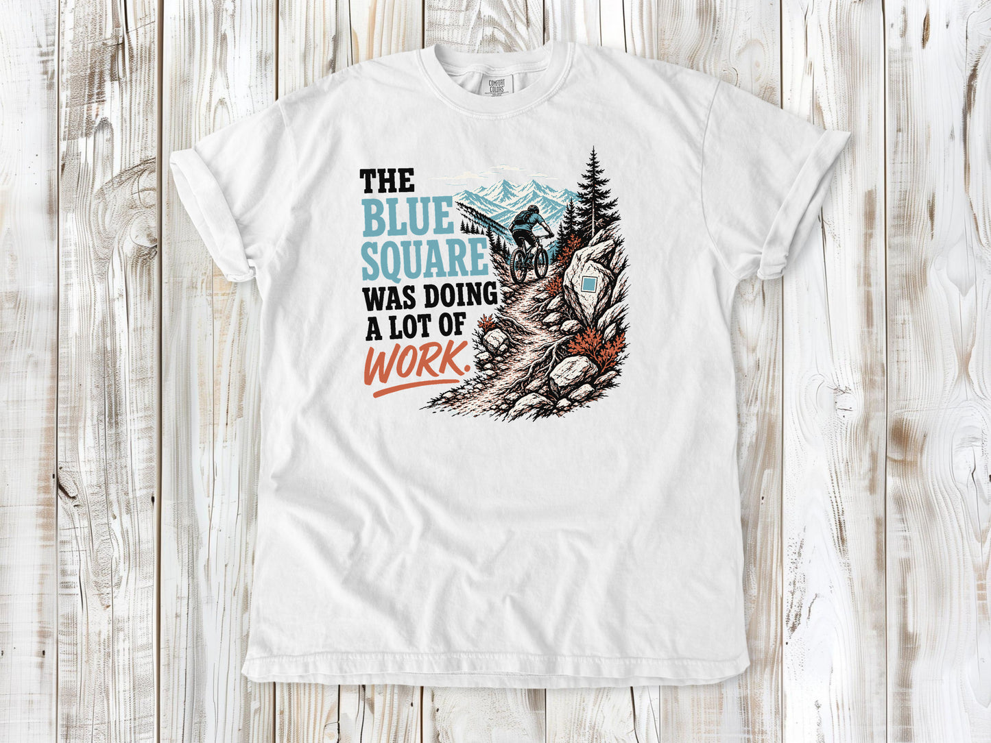 White garment-dyed tee with The Blue Square Was Doing a Lot of Work mountain bike trail graphic.