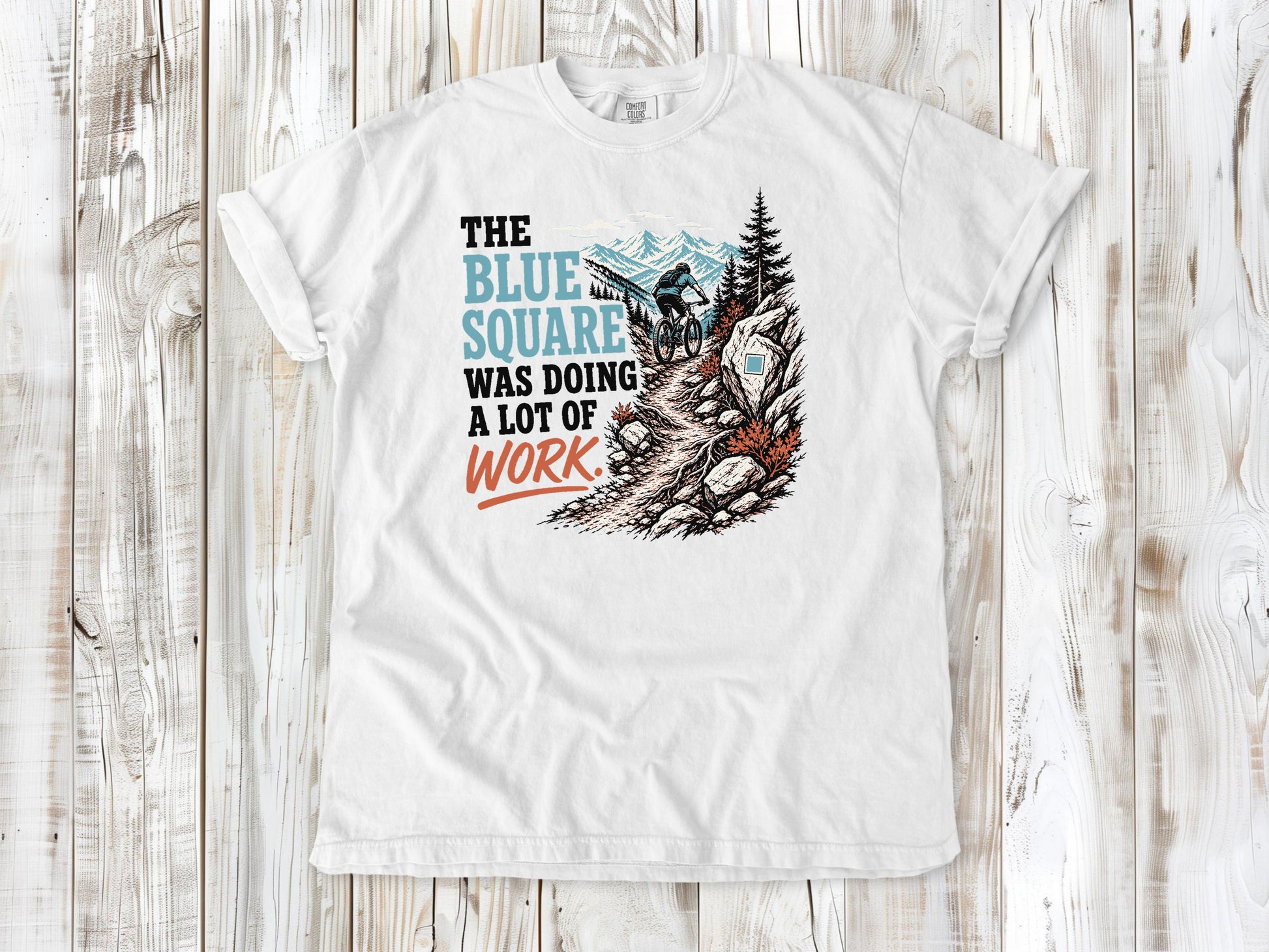 White garment-dyed tee with The Blue Square Was Doing a Lot of Work mountain bike trail graphic.