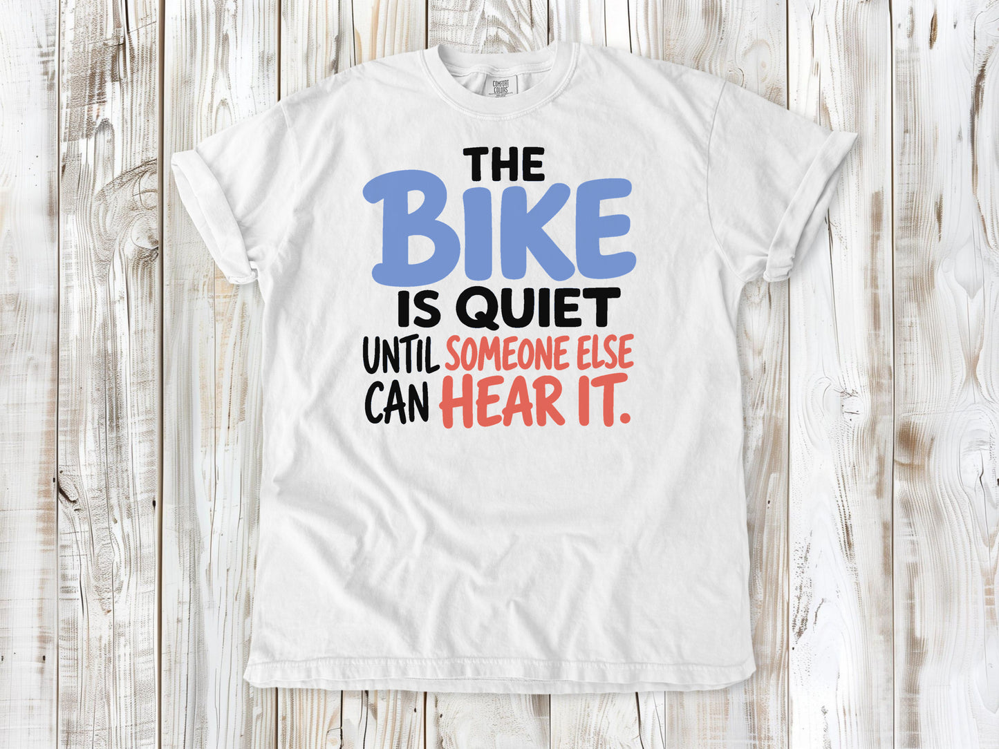 White garment-dyed tee with The Bike Is Quiet Until Someone Else Can Hear It cycling graphic.