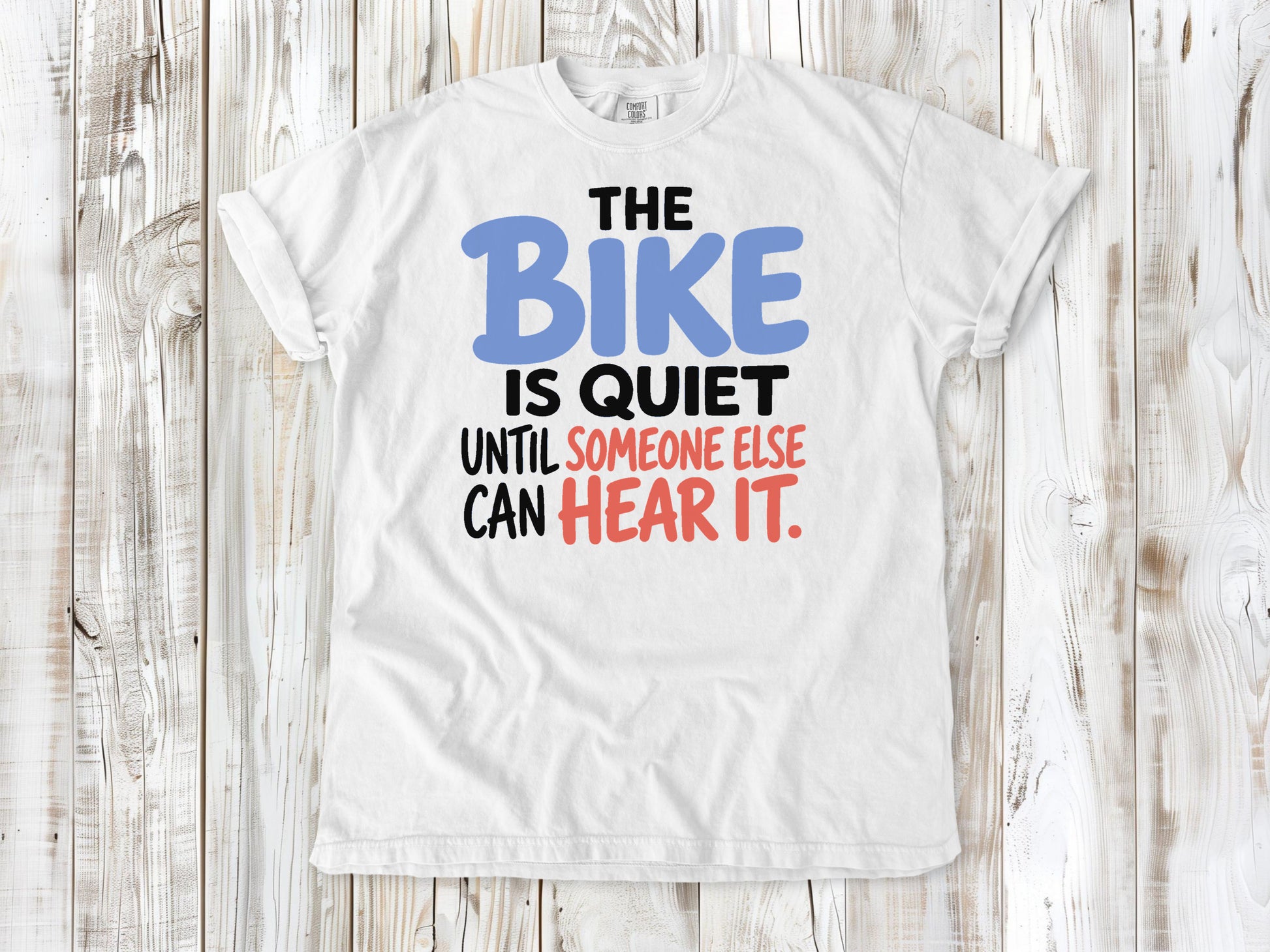 White garment-dyed tee with The Bike Is Quiet Until Someone Else Can Hear It cycling graphic.
