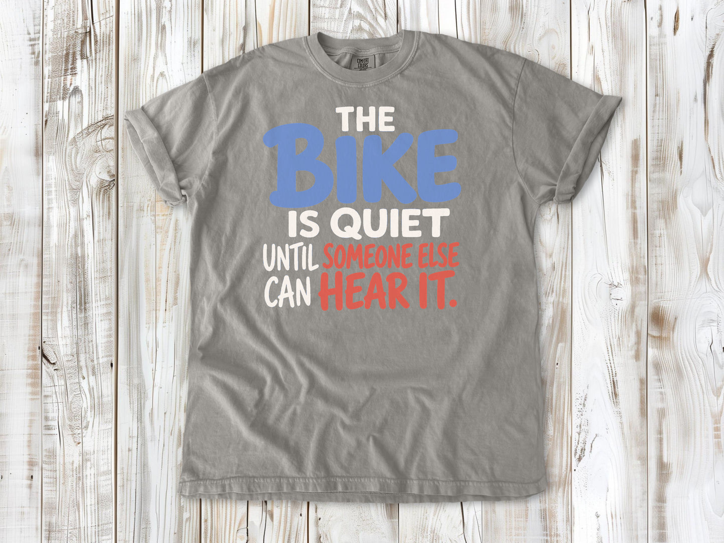 Khaki garment-dyed tee with The Bike Is Quiet Until Someone Else Can Hear It cycling graphic.