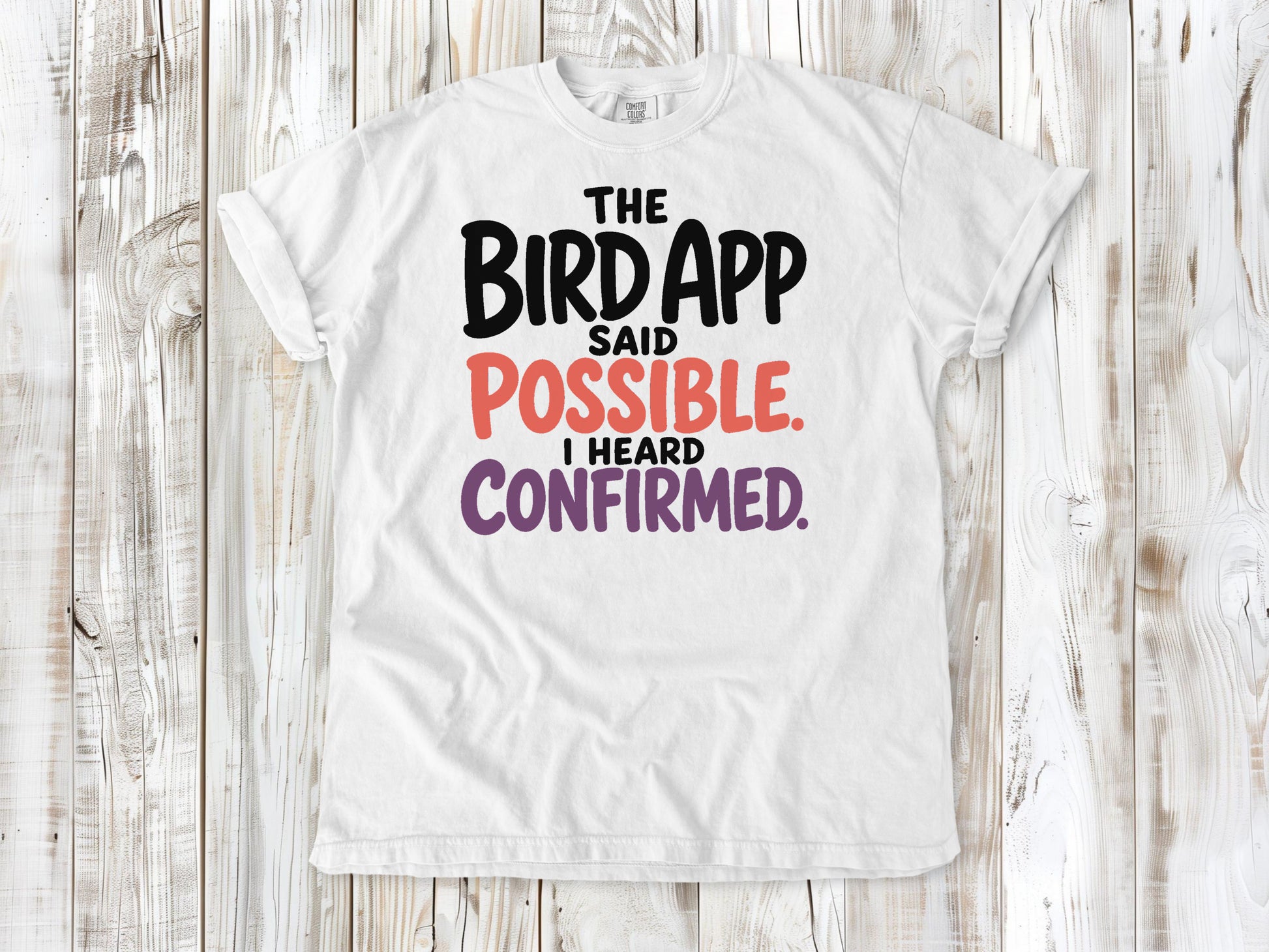 White garment-dyed tee with The Bird App Said Possible I Heard Confirmed birding graphic.