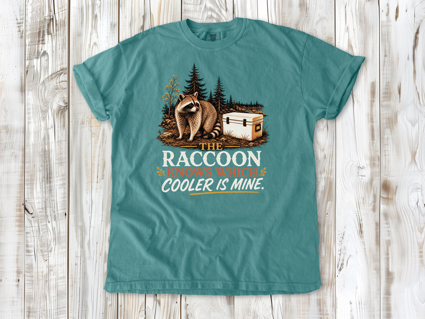 Mustard garment-dyed tee with The Raccoon Knows Which Cooler Is Mine camping graphic.