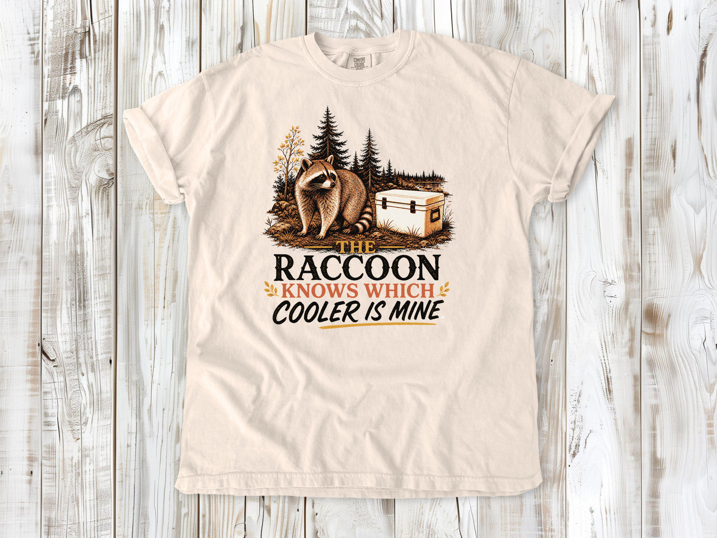 Butter garment-dyed tee with The Raccoon Knows Which Cooler Is Mine camping graphic.