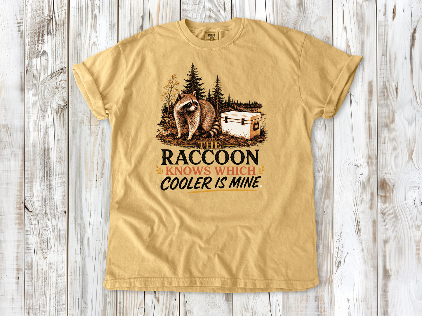 Burnt Orange garment-dyed tee with The Raccoon Knows Which Cooler Is Mine camping graphic.