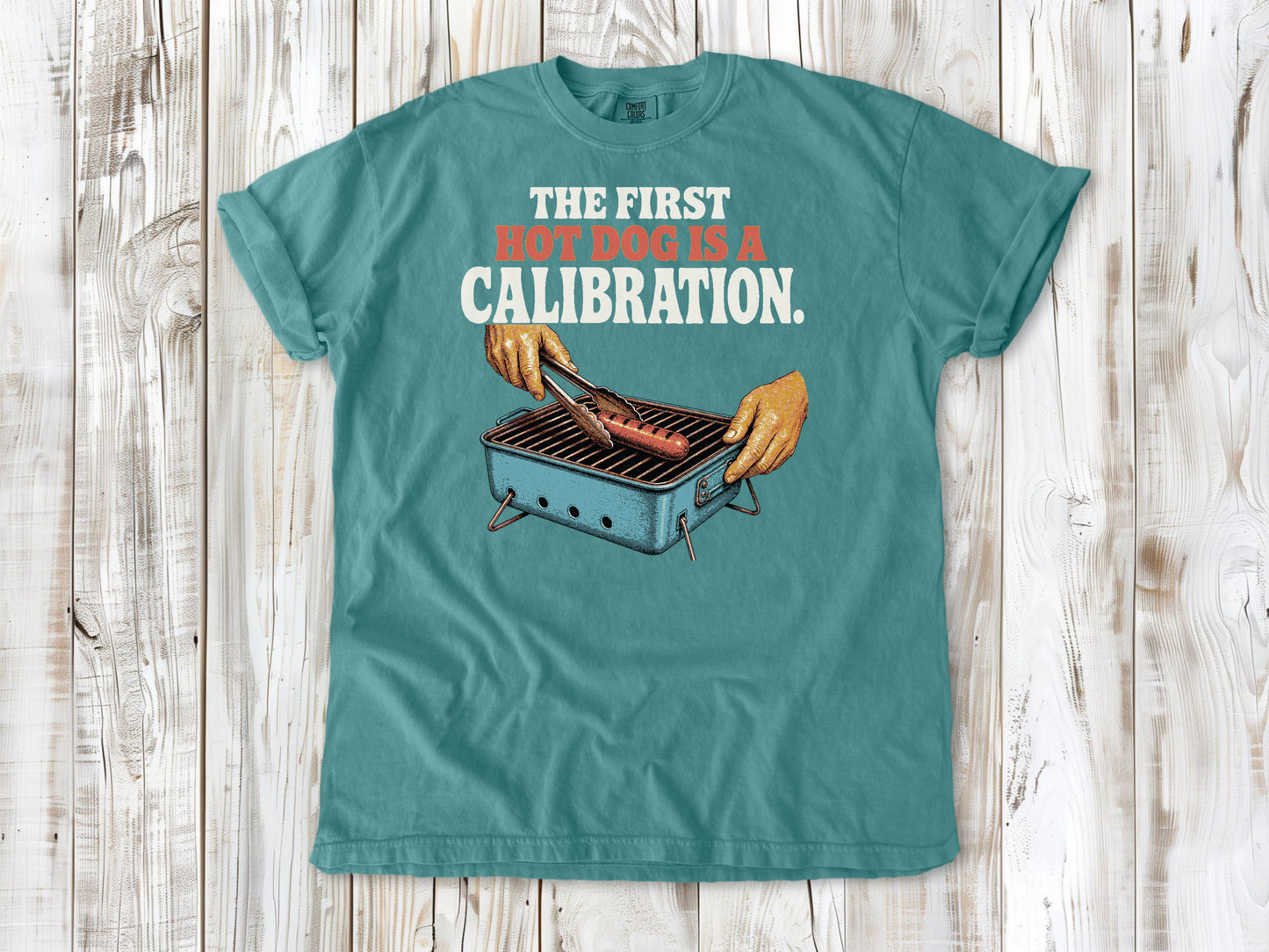 Mustard garment-dyed tee with The First Hot Dog Is a Calibration beach grilling graphic.