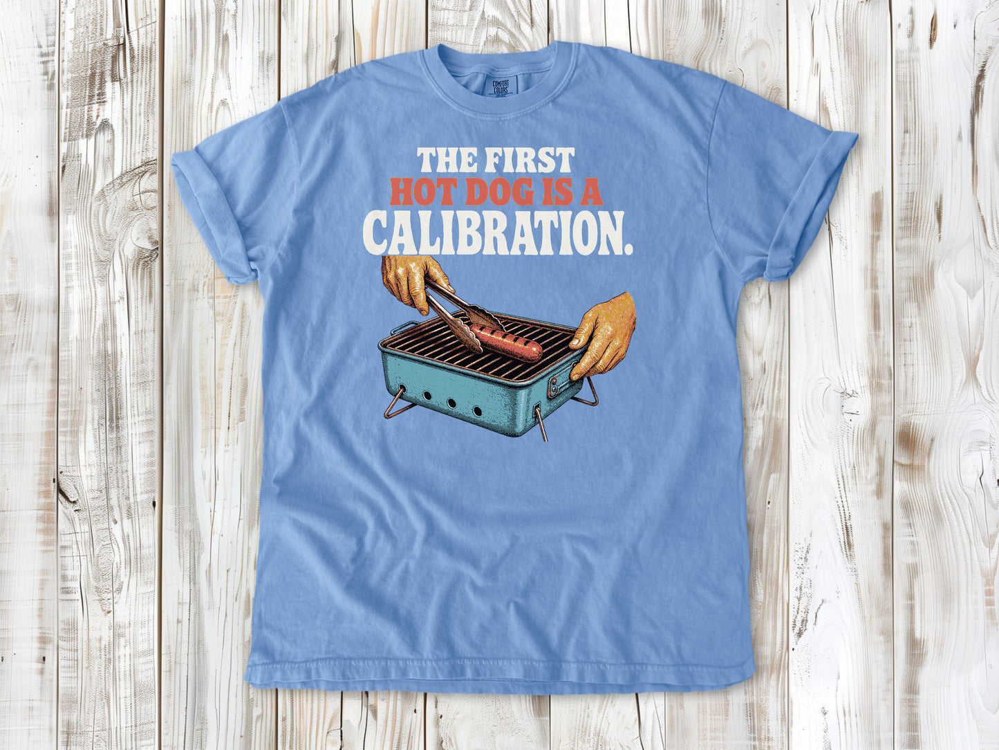Pepper garment-dyed tee with The First Hot Dog Is a Calibration beach grilling graphic.