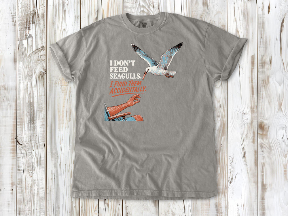 Khaki garment-dyed tee with I Don't Feed Seagulls I Fund Them Accidentally beach graphic.