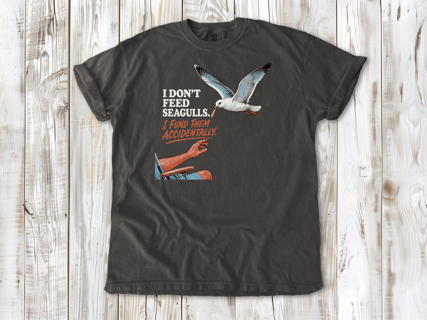 Ivory garment-dyed tee with I Don't Feed Seagulls I Fund Them Accidentally beach graphic.