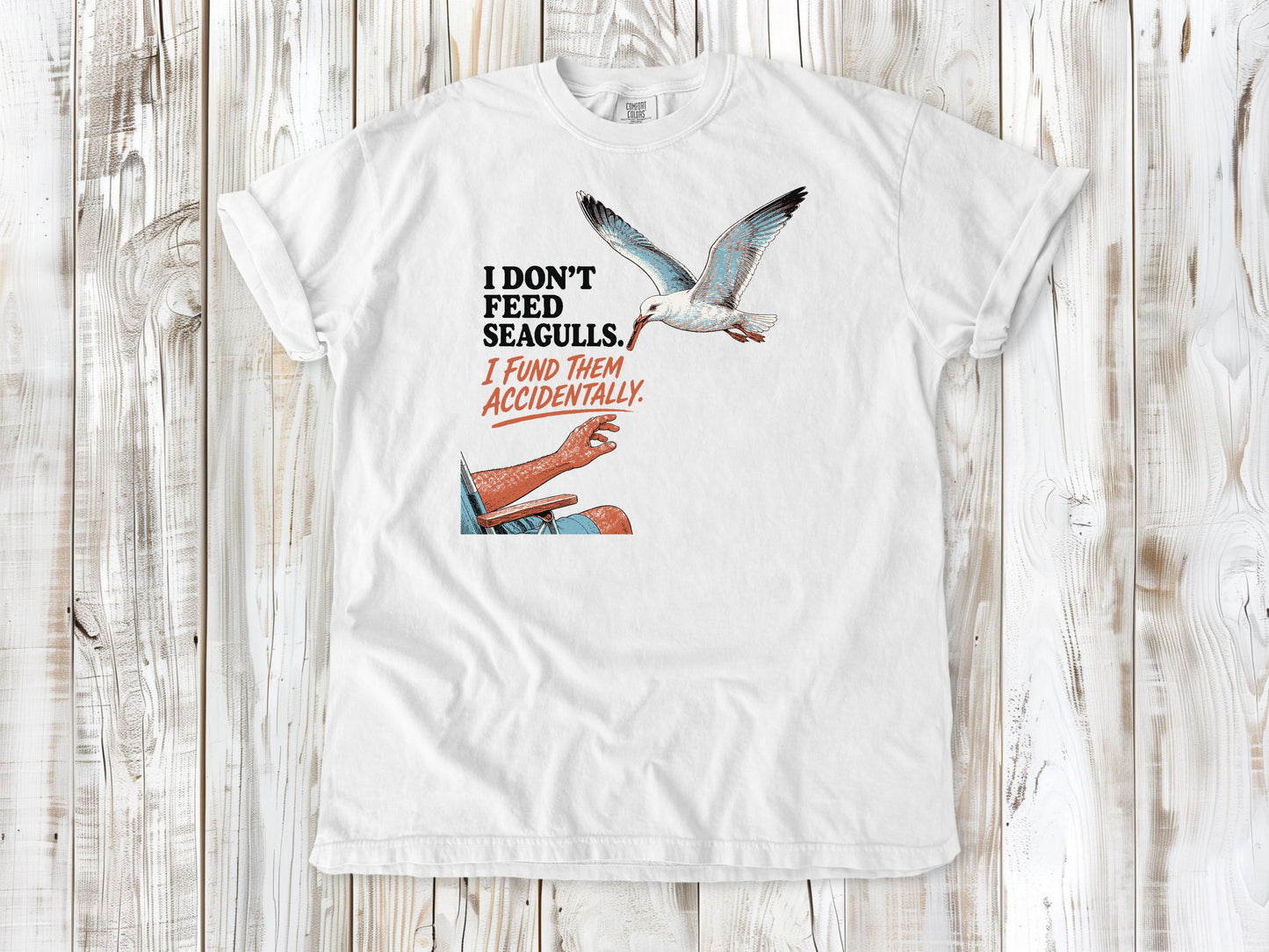 White garment-dyed tee with I Don't Feed Seagulls I Fund Them Accidentally beach graphic.