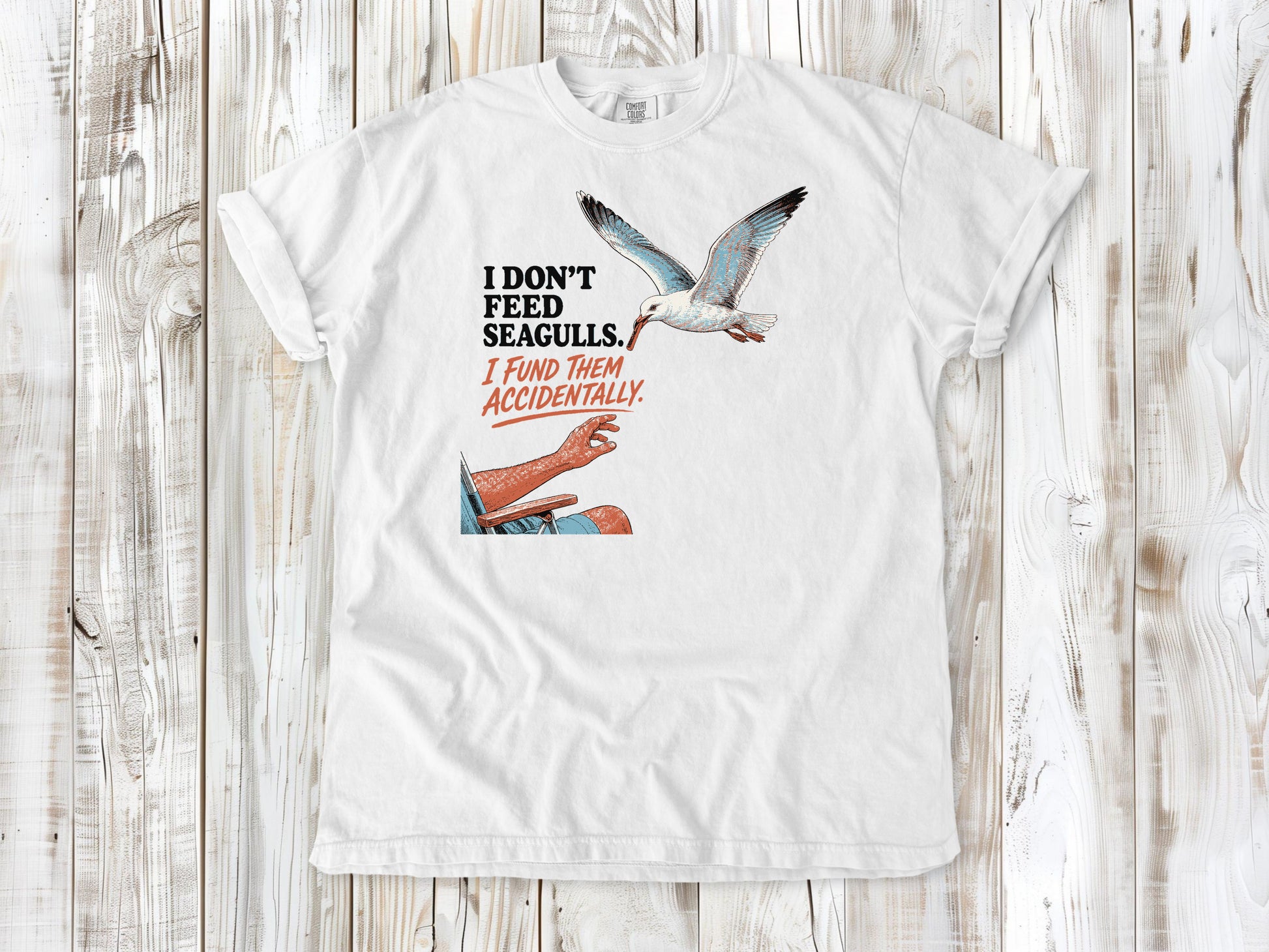 White garment-dyed tee with I Don't Feed Seagulls I Fund Them Accidentally beach graphic.