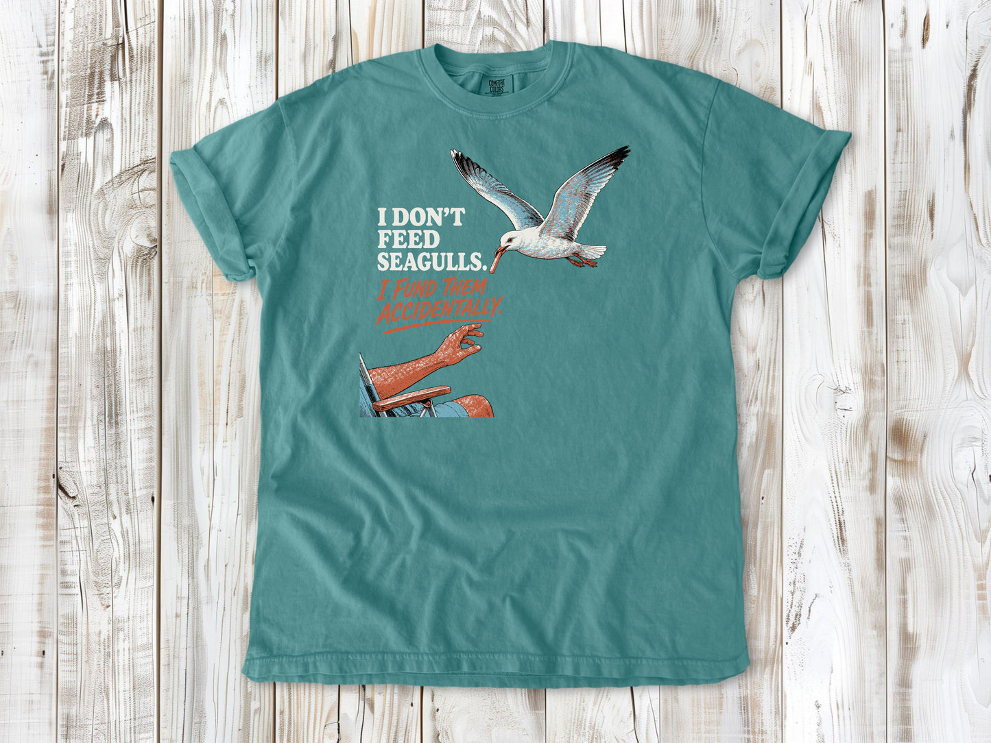 Mustard garment-dyed tee with I Don't Feed Seagulls I Fund Them Accidentally beach graphic.