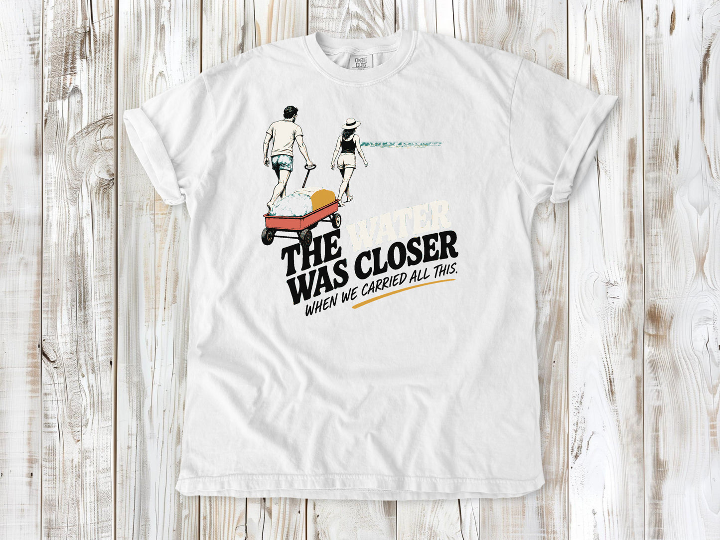 White garment-dyed tee with The Water Was Closer When We Carried All This beach graphic.