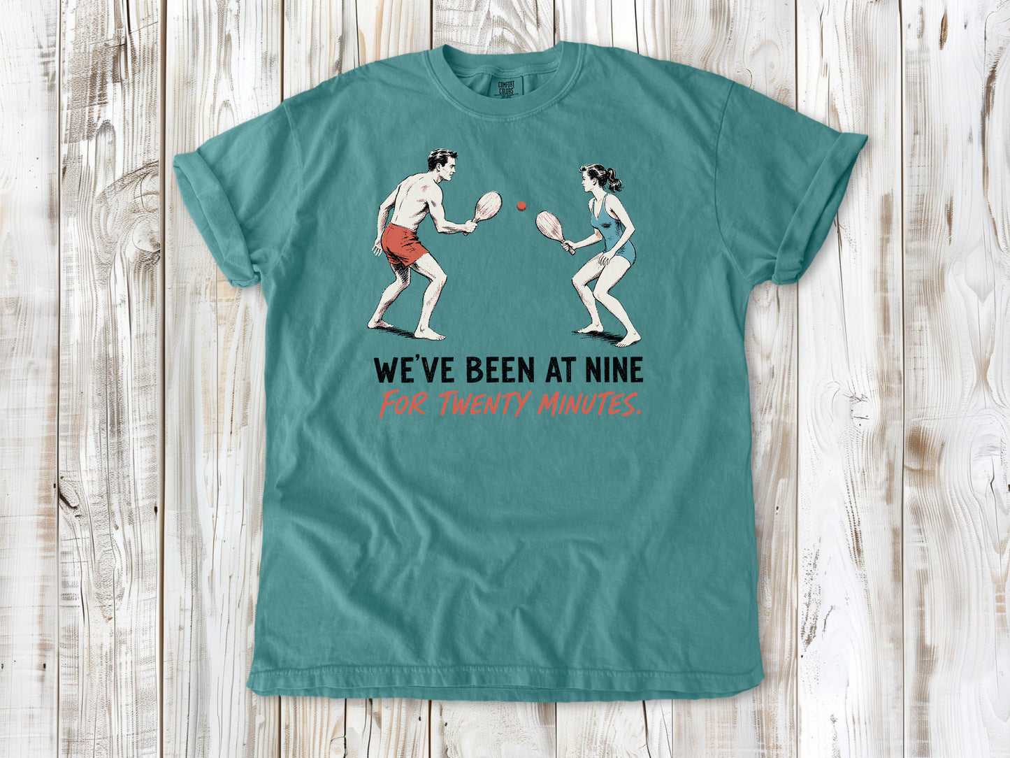 Mustard garment-dyed tee with We've Been at Nine for Twenty Minutes beach paddleball graphic.