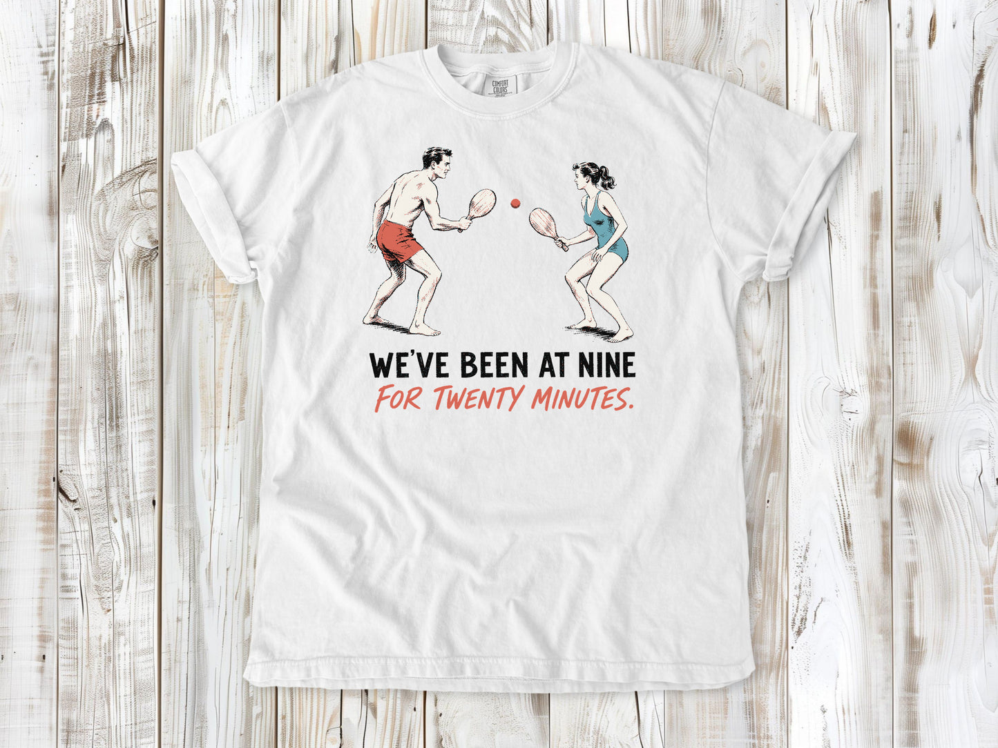 White garment-dyed tee with We've Been at Nine for Twenty Minutes beach paddleball graphic.