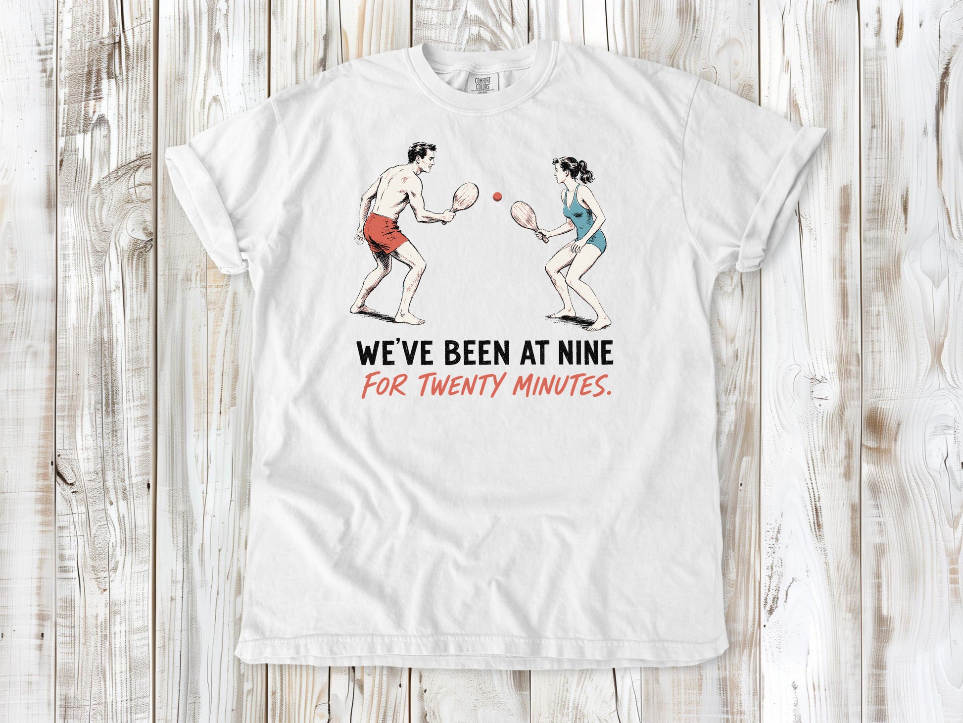 White garment-dyed tee with We've Been at Nine for Twenty Minutes beach paddleball graphic.