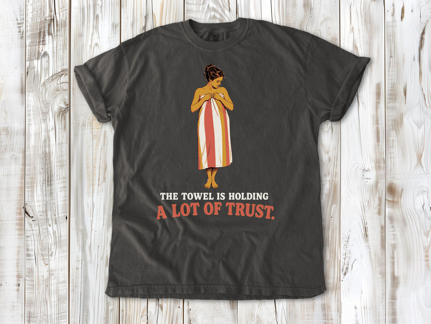 Ivory garment-dyed tee with The Towel Is Holding a Lot of Trust beach graphic.