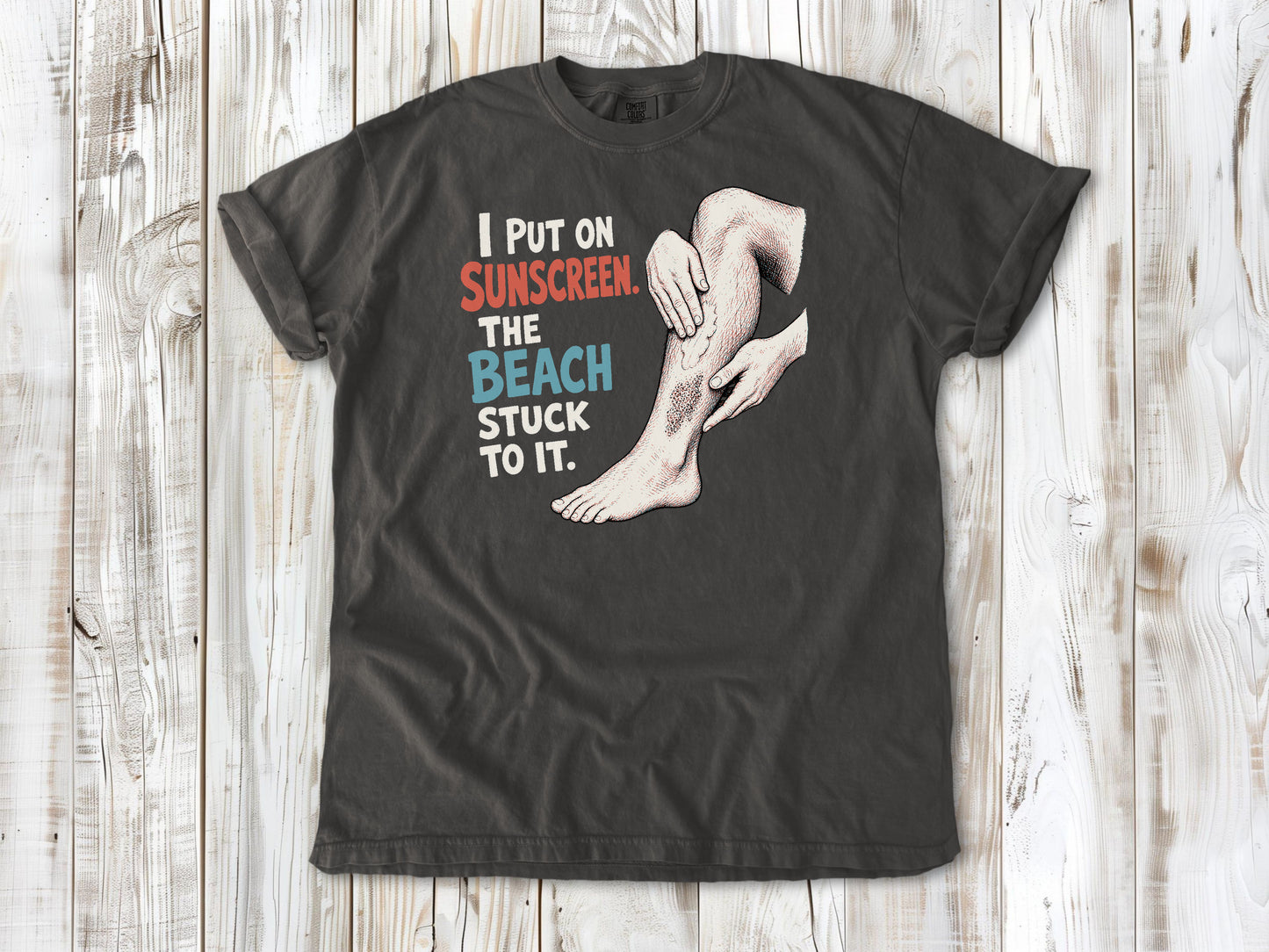 Ivory garment-dyed tee with I Put on Sunscreen The Beach Stuck to It graphic.