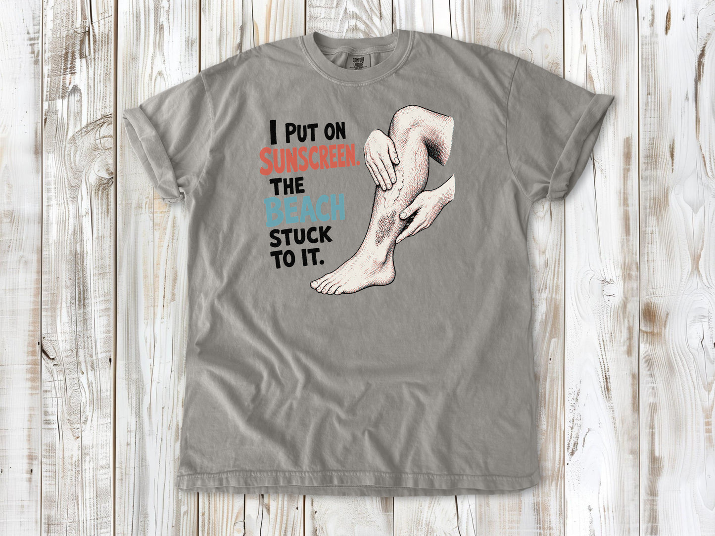 Khaki garment-dyed tee with I Put on Sunscreen The Beach Stuck to It graphic.
