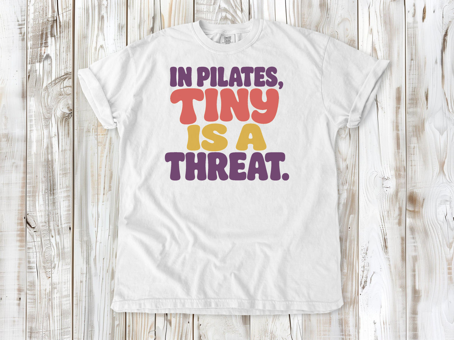 White garment-dyed tee with In Pilates Tiny Is a Threat studio humor graphic.