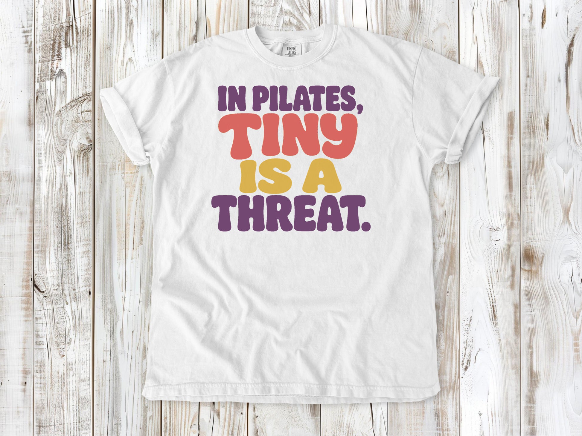 White garment-dyed tee with In Pilates Tiny Is a Threat studio humor graphic.