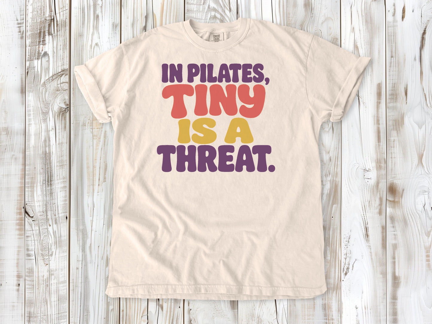 Ivory garment-dyed tee with In Pilates Tiny Is a Threat studio humor graphic.