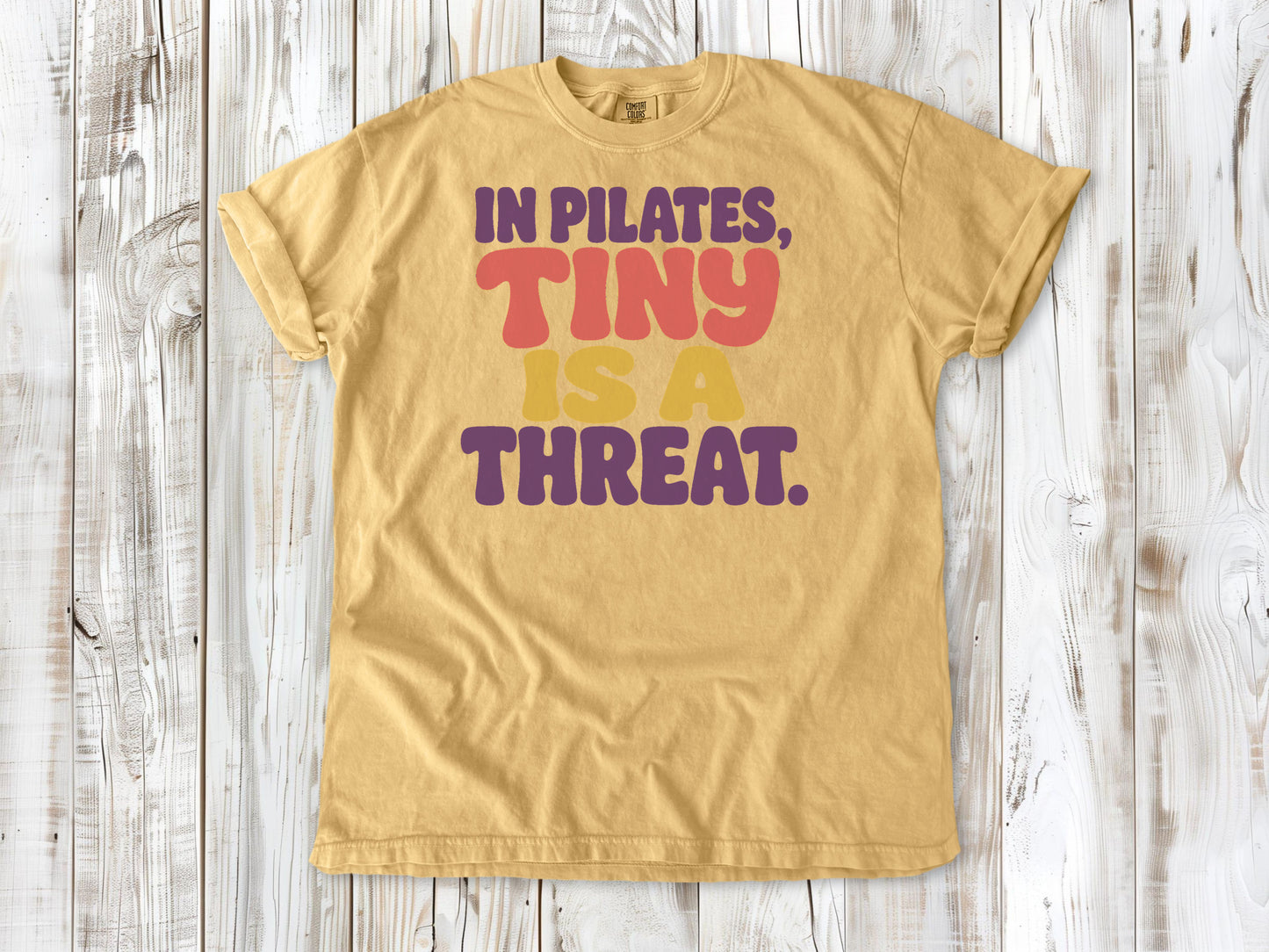 Mustard garment-dyed tee with In Pilates Tiny Is a Threat studio humor graphic.