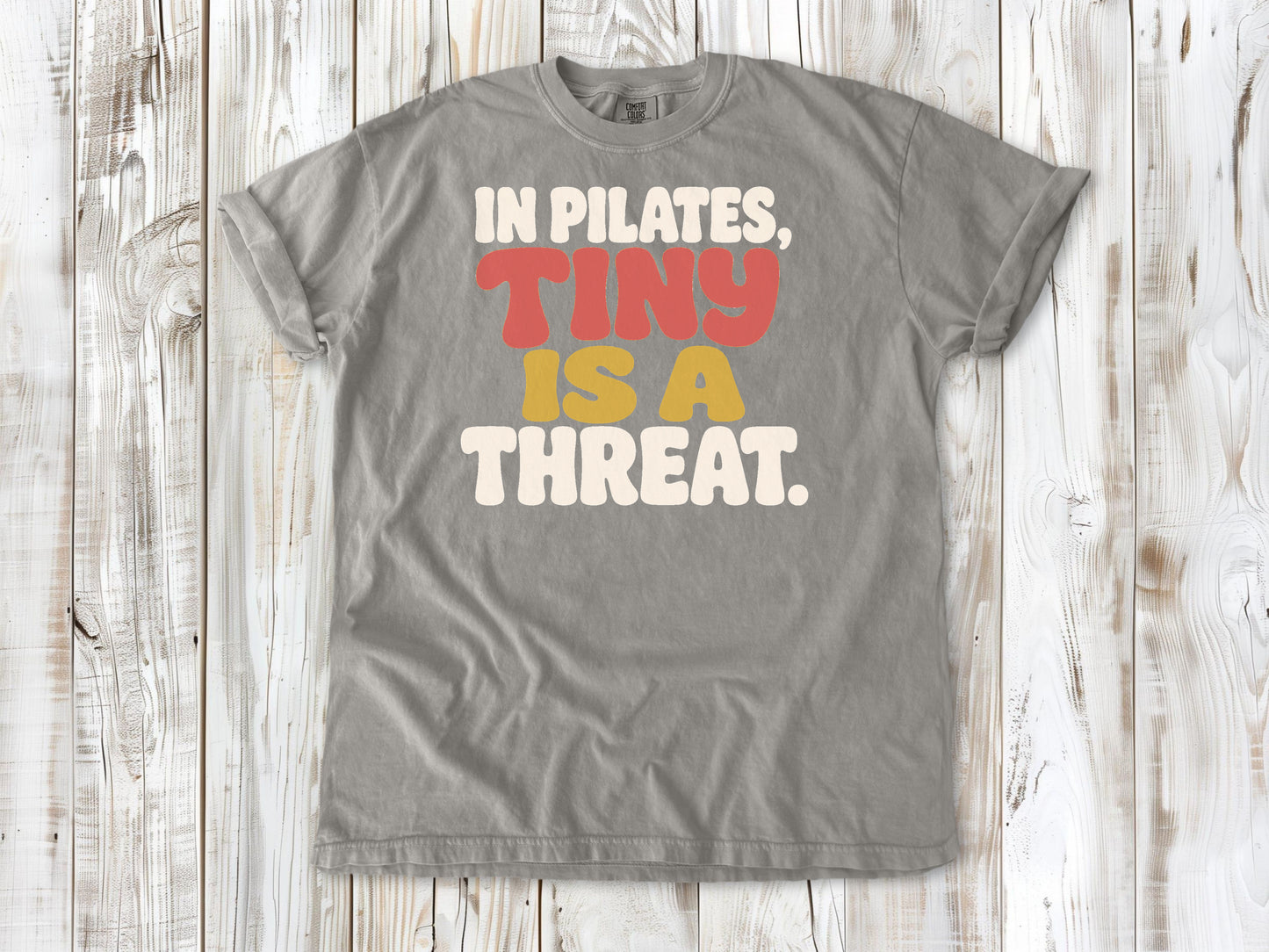 Grey garment-dyed tee with In Pilates Tiny Is a Threat studio humor graphic.