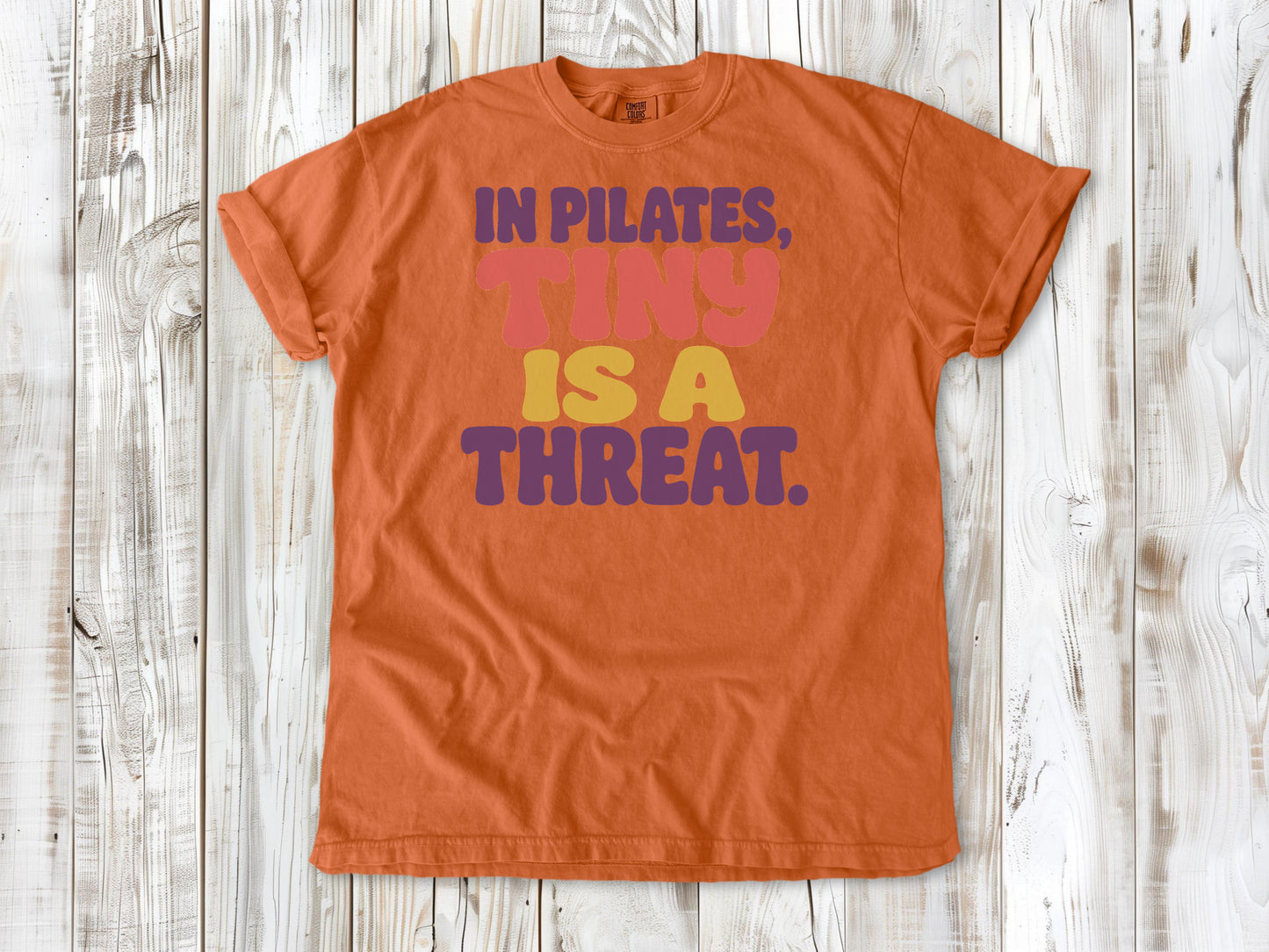 Burnt Orange garment-dyed tee with In Pilates Tiny Is a Threat studio humor graphic.