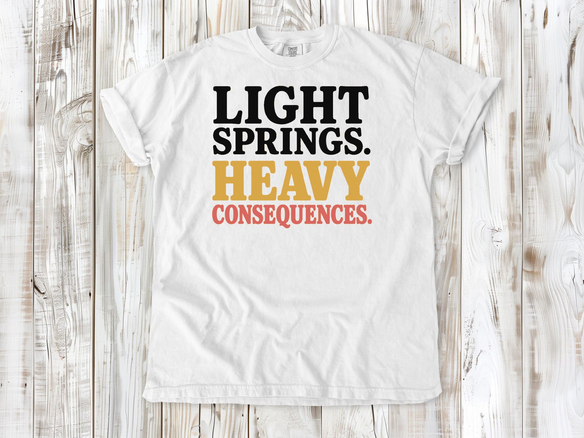 White garment-dyed tee with Light Springs Heavy Consequences reformer Pilates graphic.